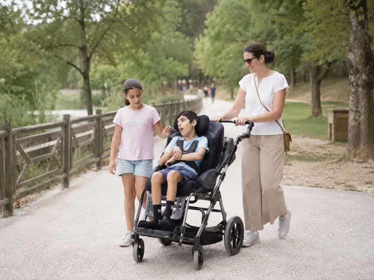 Un adolescent en situation de polyhandicap se promène en fauteuil roulant entouré de sa famille