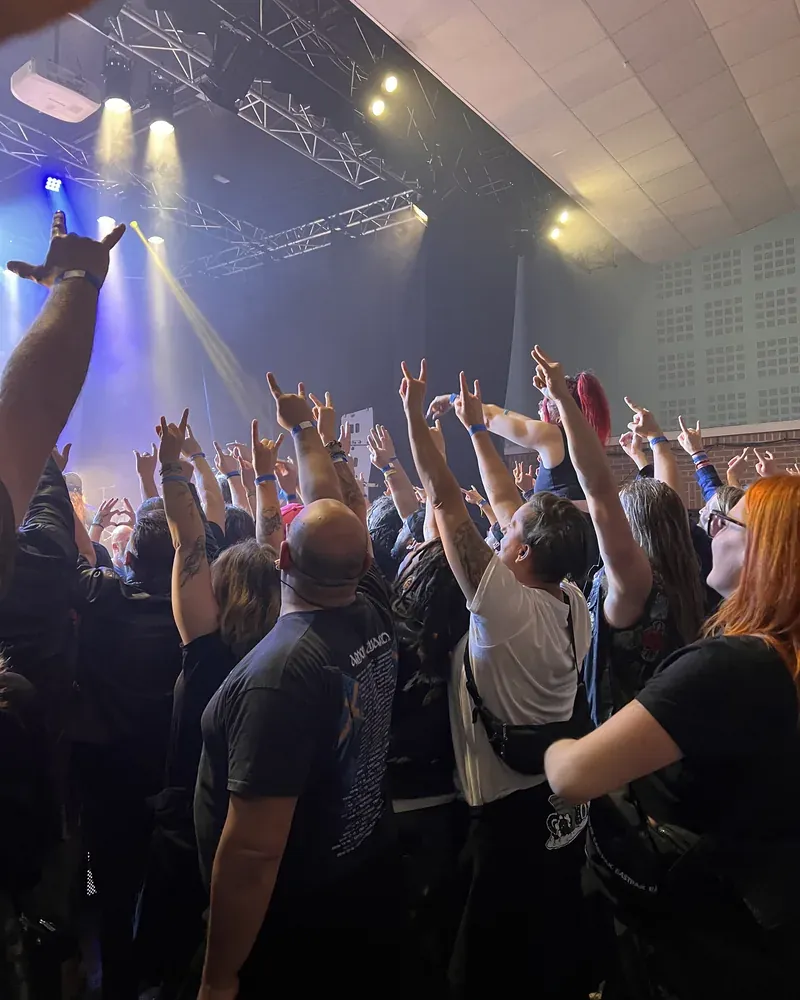 Une foule de festivaliers, mains levées devant la scène et ses jeux de lumière, lors d'un concert de metal soutenu par le Réseau AUXI'life dans le cadre de son mécénat