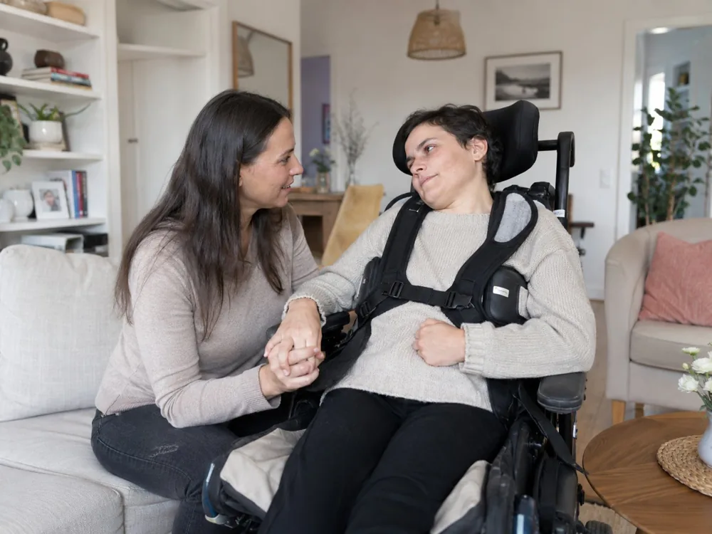 Deux femmes, l'une en fauteuil roulant, partagent un moment de complicité dans leur salon